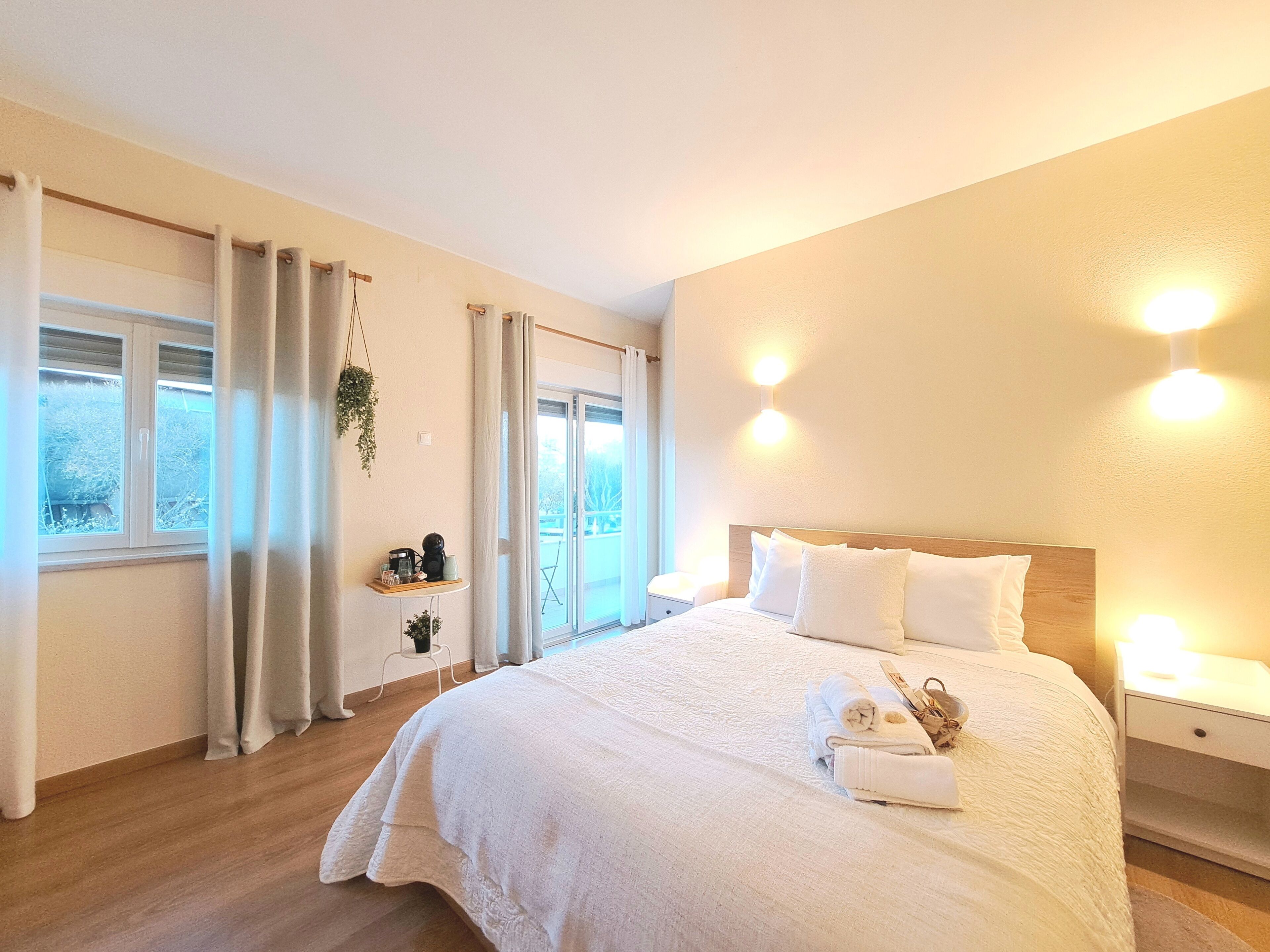 A bedroom with a large bed, bedside tables, a window with curtains, and a view of the outdoors.