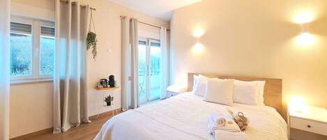 A bedroom with a large bed, bedside tables, a window with curtains, and a view of the outdoors.