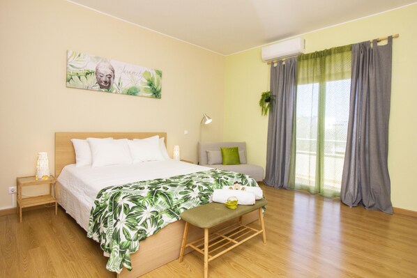 Une chambre à coucher comprenant un lit, une table de chevet, un banc et une fenêtre avec des rideaux.