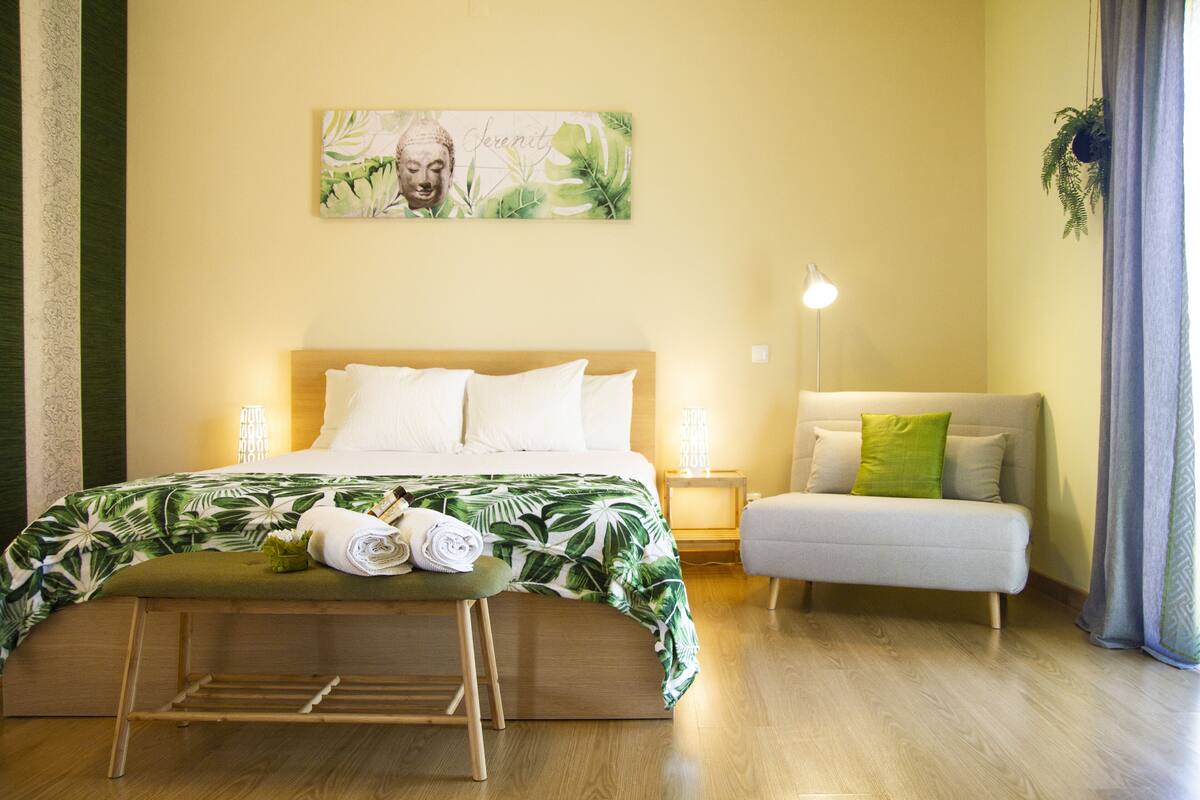 Ein ordentlich eingerichtetes Schlafzimmer mit Bett, Nachttischen, einer Couch und einem Wandbild.