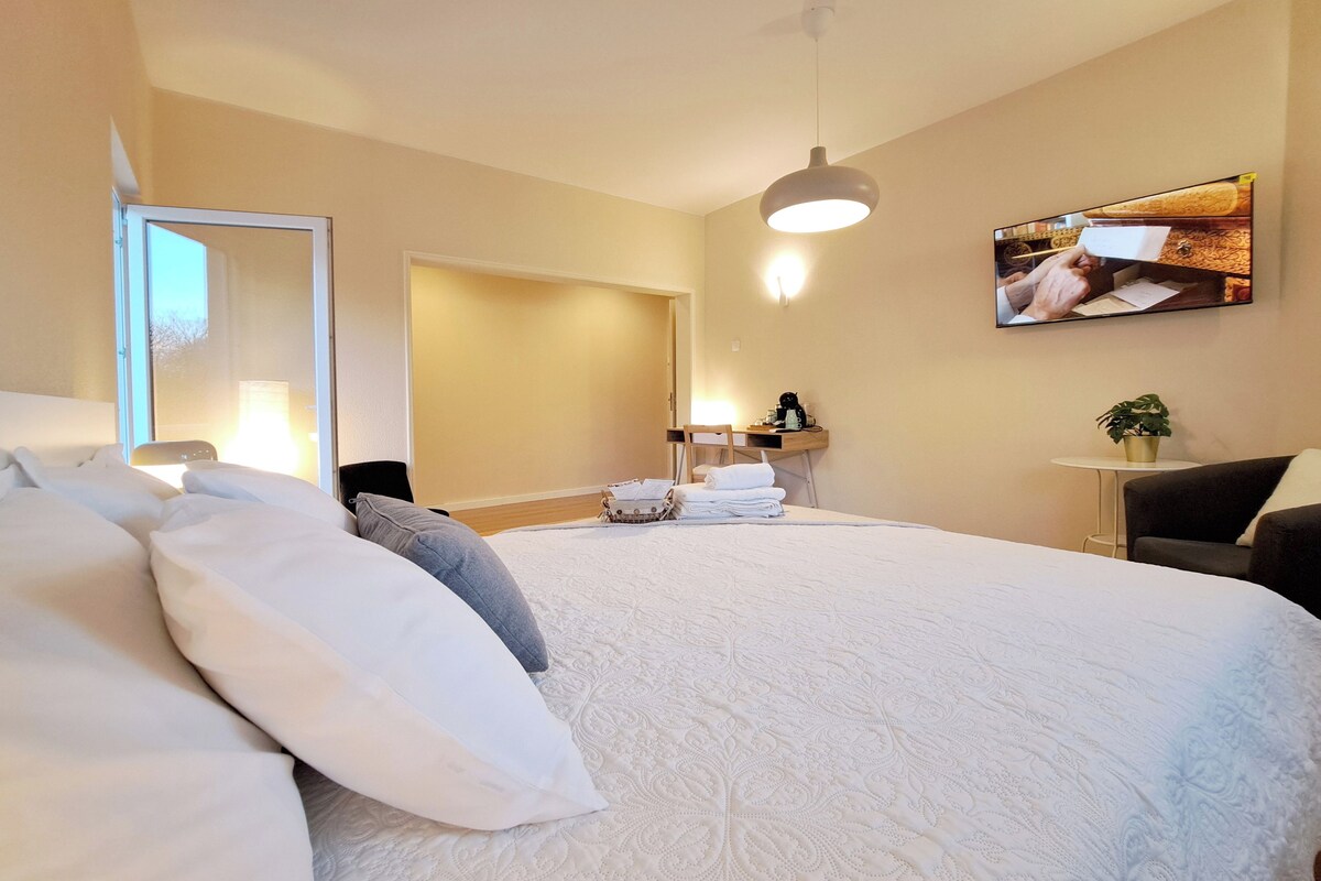 Hotelkamer met een groot bed, een flatscreen televisie aan de muur, een klein tafeltje met een plant en een spiegel op de deur.