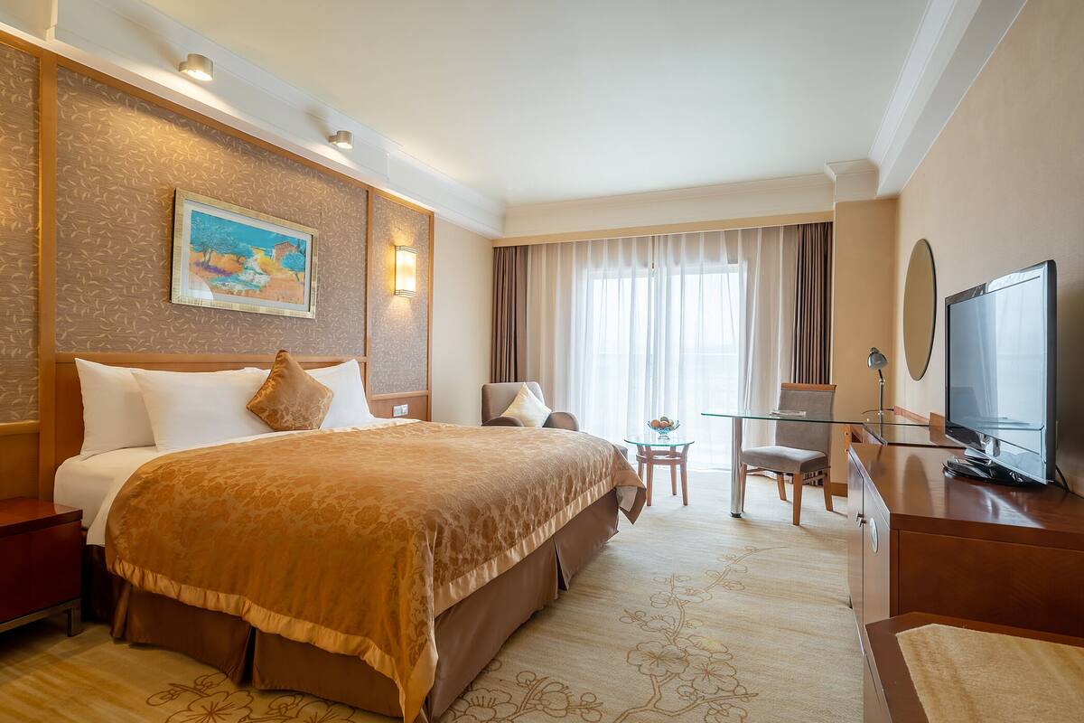 A hotel room with a large bed, a desk with a chair, a television, and a painting on the wall.