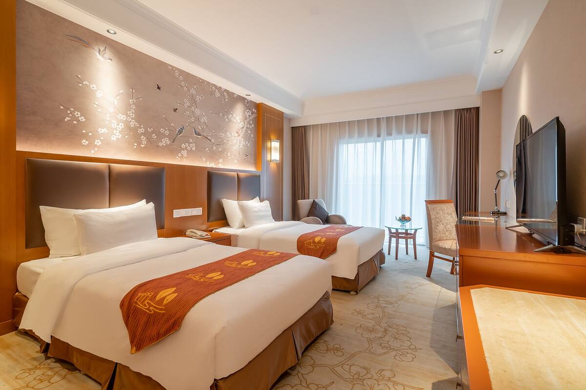 A hotel room with two beds, a desk, a chair, and a TV.