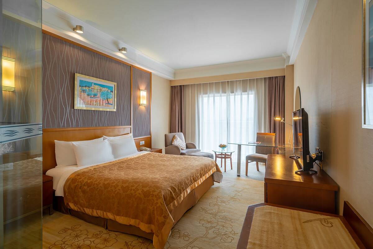 A hotel room with a large bed, a desk with a chair, a television, and a painting on the wall.