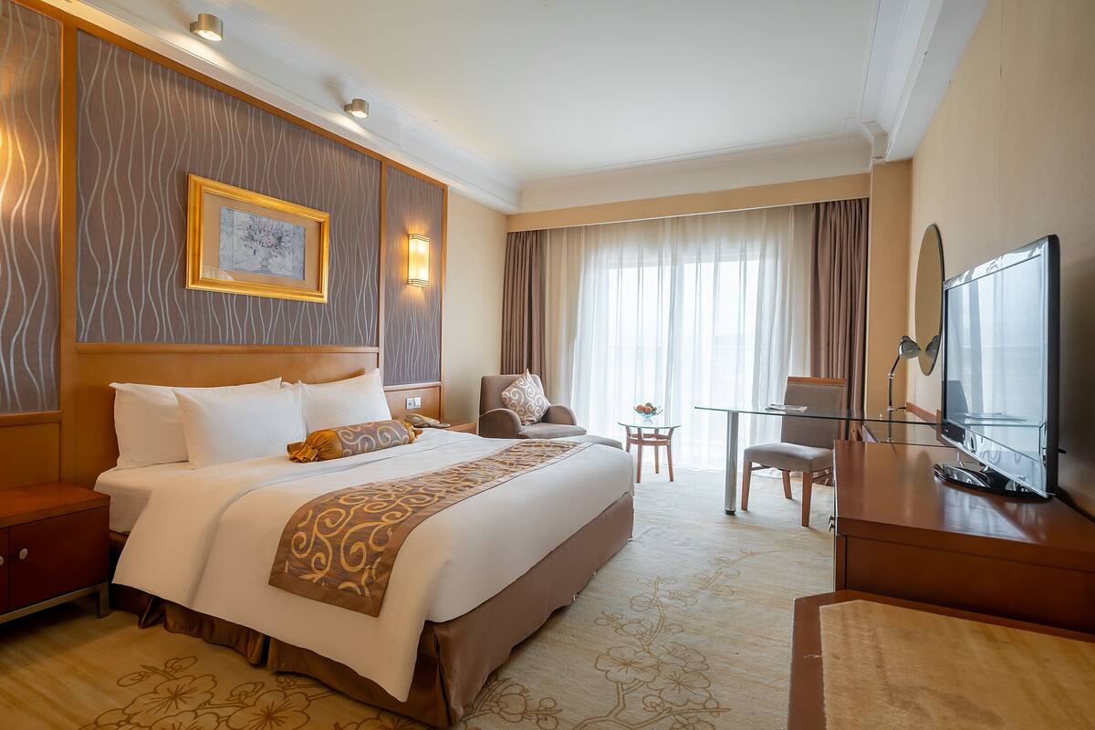 A hotel room with a large bed, a desk, a chair, a television, and a window with curtains.