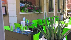 An outdoor cafe with green chairs and tables, potted plants, and a menu stand. - Au Cheval Blanc (Saint-Amarin)