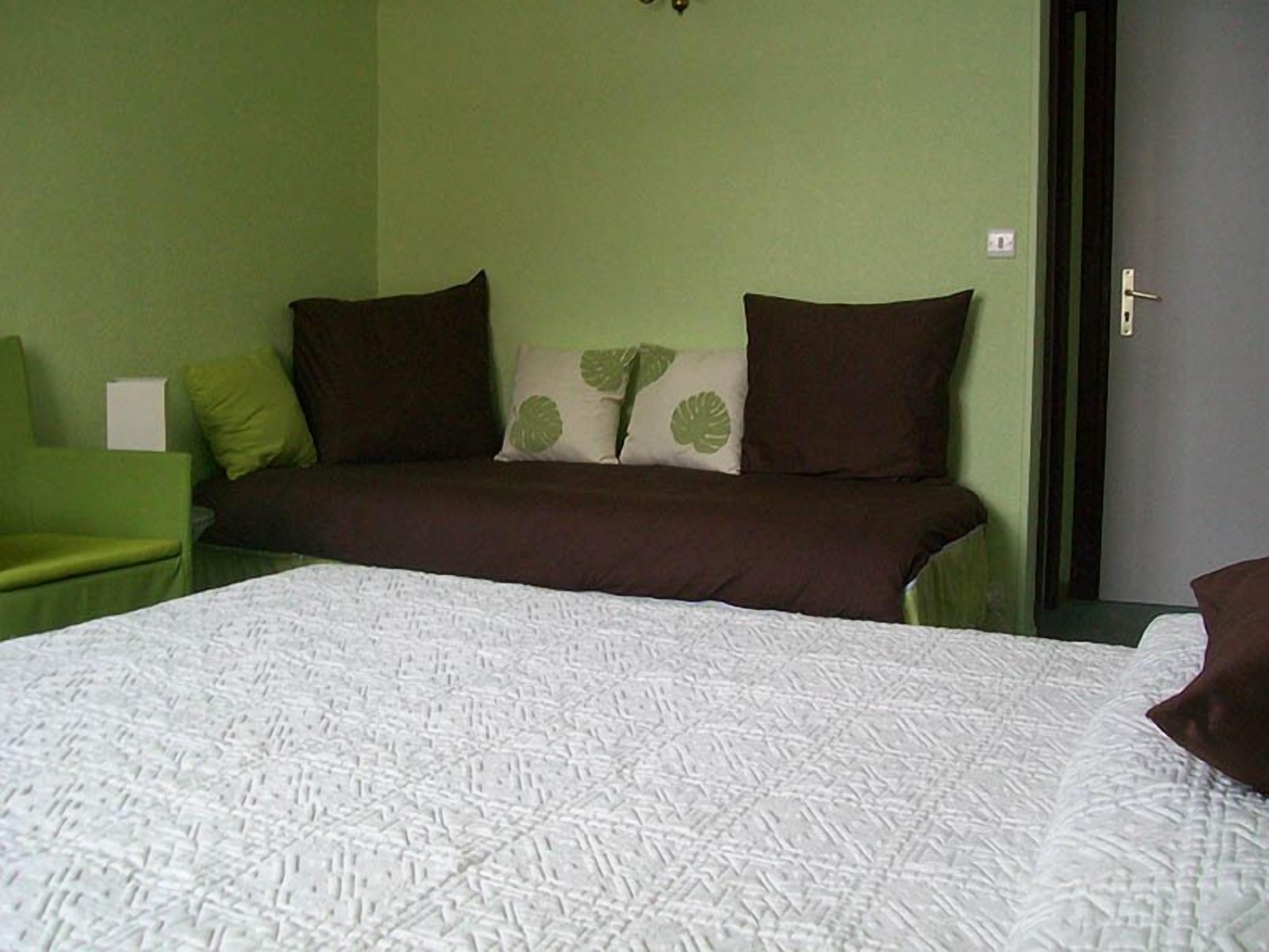 Een kamer met een bed, een groene fauteuil en een deur.
