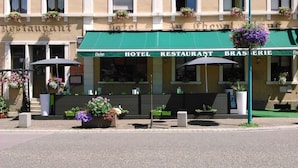 A hotel with a green awning, outdoor seating, and flower planters. - Au Cheval Blanc (Saint-Amarin)