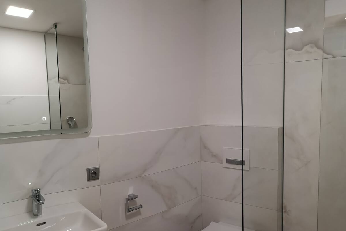 A modern bathroom with a white sink, a toilet, and a glass-enclosed shower.