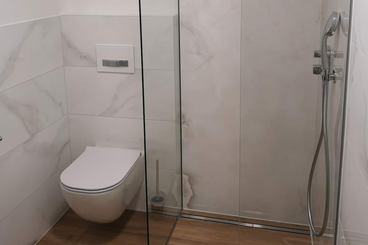 A modern bathroom with a glass shower enclosure, a toilet, and a visible control panel.