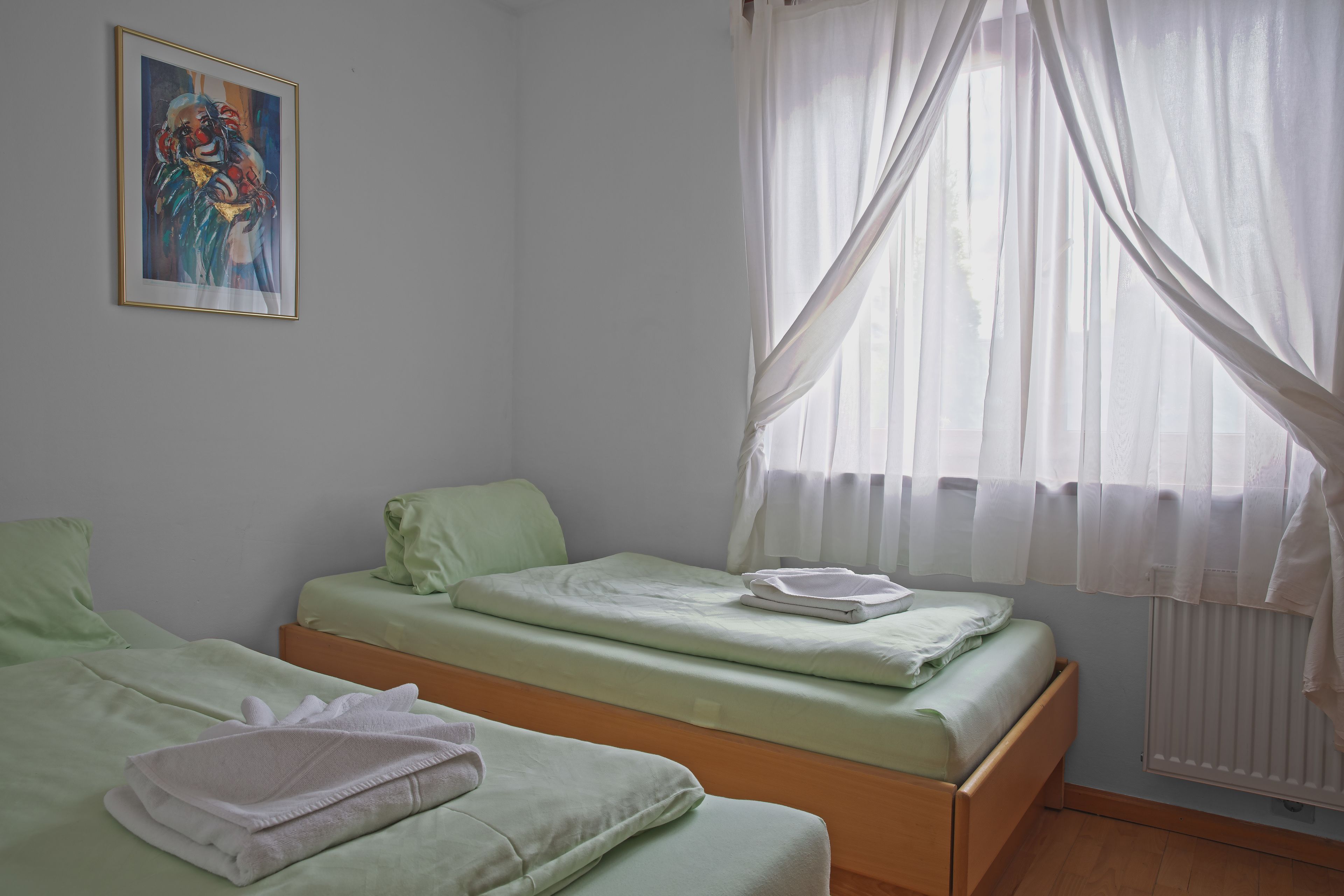 Une chambre avec deux lits simples, un radiateur et une fenêtre avec des rideaux légers.
