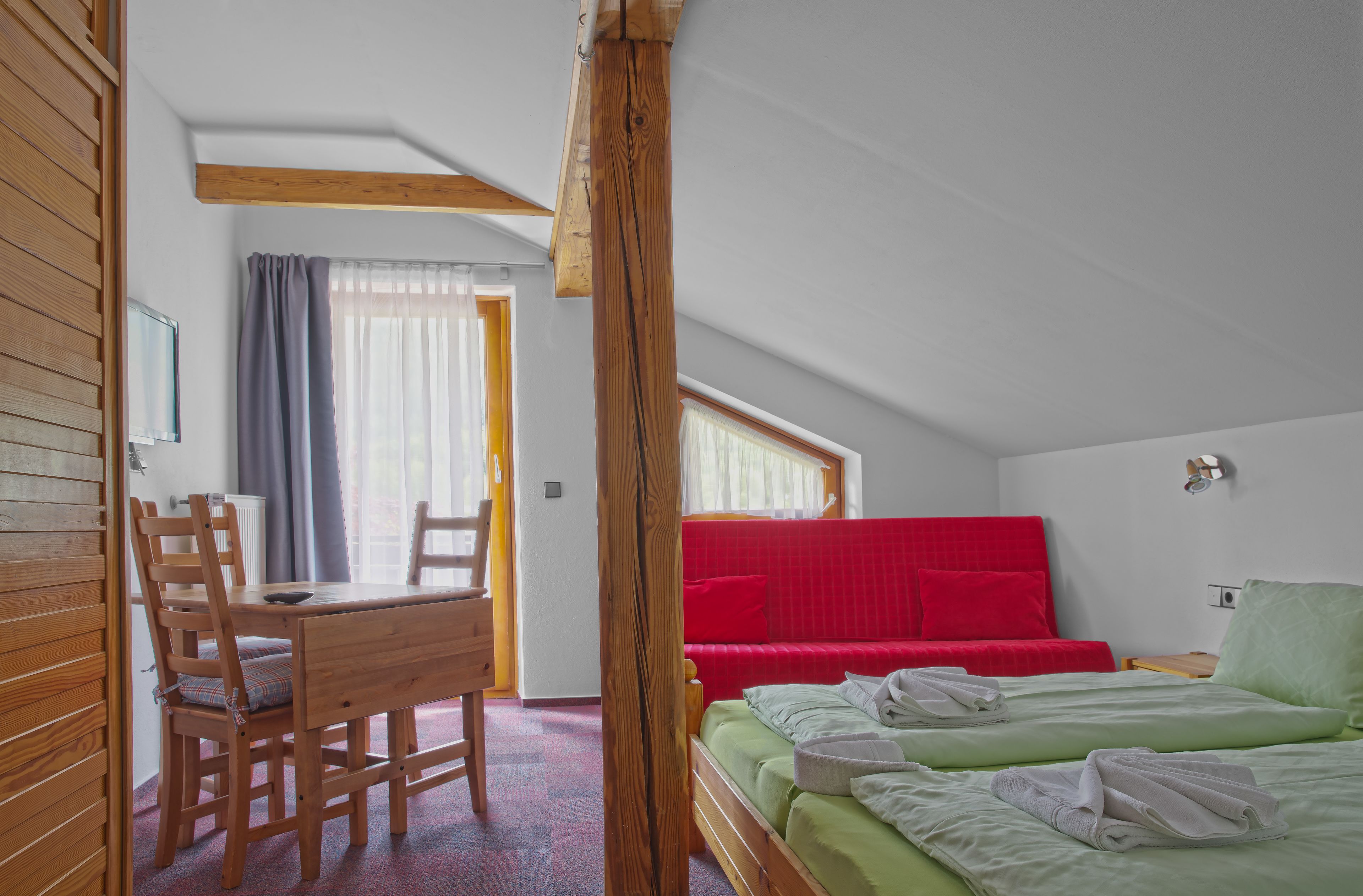 Un dormitorio con una cama, un sofá rojo, una mesa de madera y una silla.