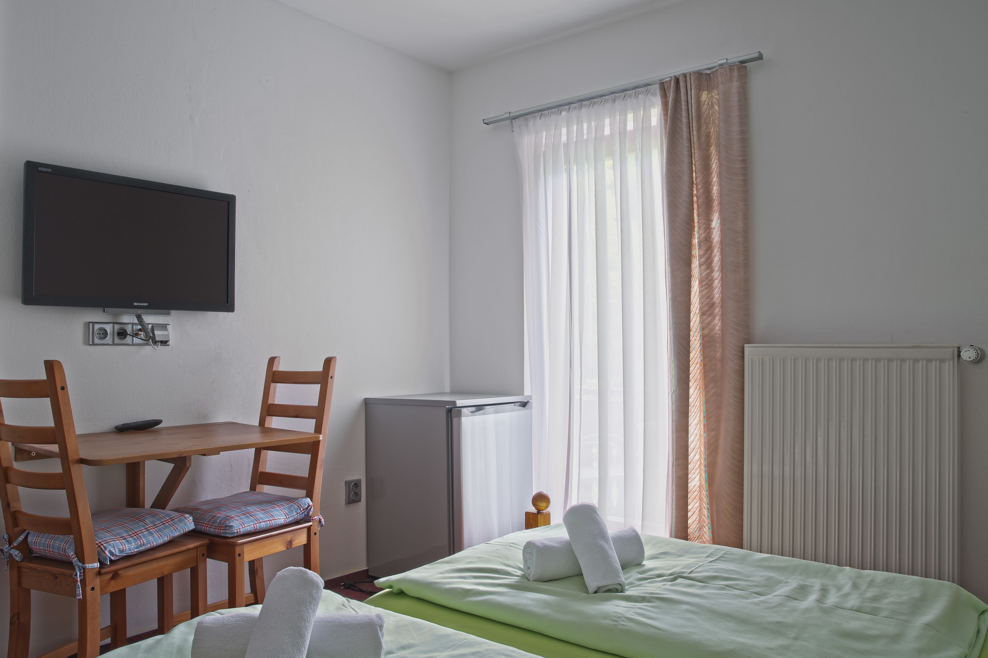 A hotel room with a bed, a desk with a chair, a television, a radiator, and curtains.