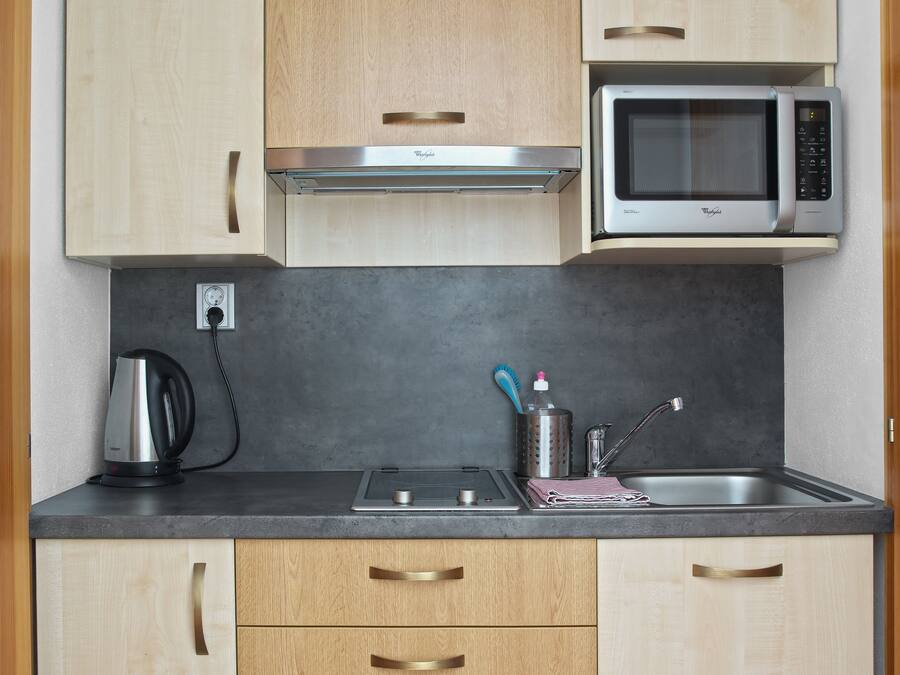 A compact kitchen with wooden cabinets, a built-in microwave, a kettle, and a sink with modern faucets.