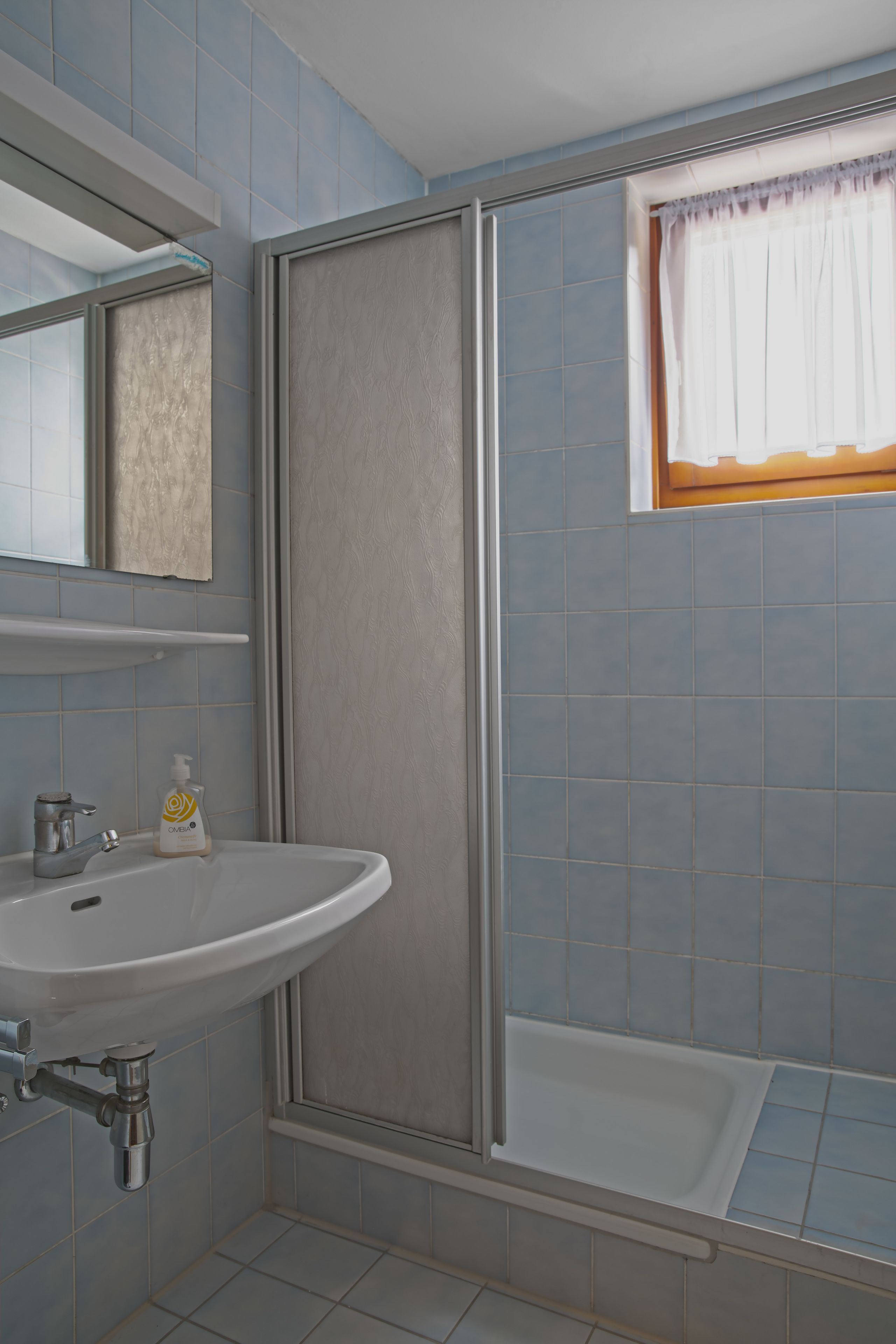 A bathroom with a sink, mirror, shower, and a window with a curtain.