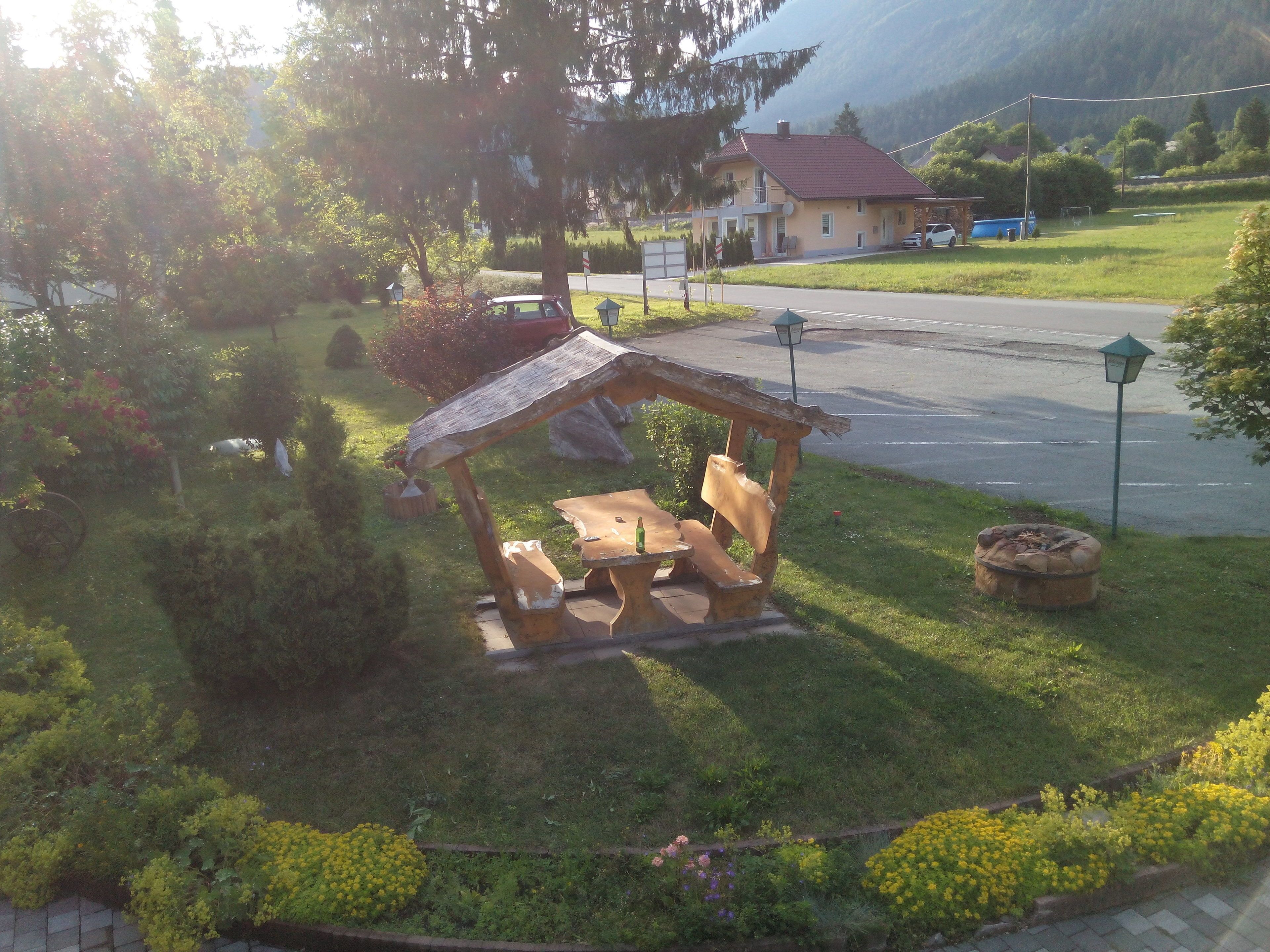 A gazebo with benches and a fire pit in a grassy area with a road and houses in the background.