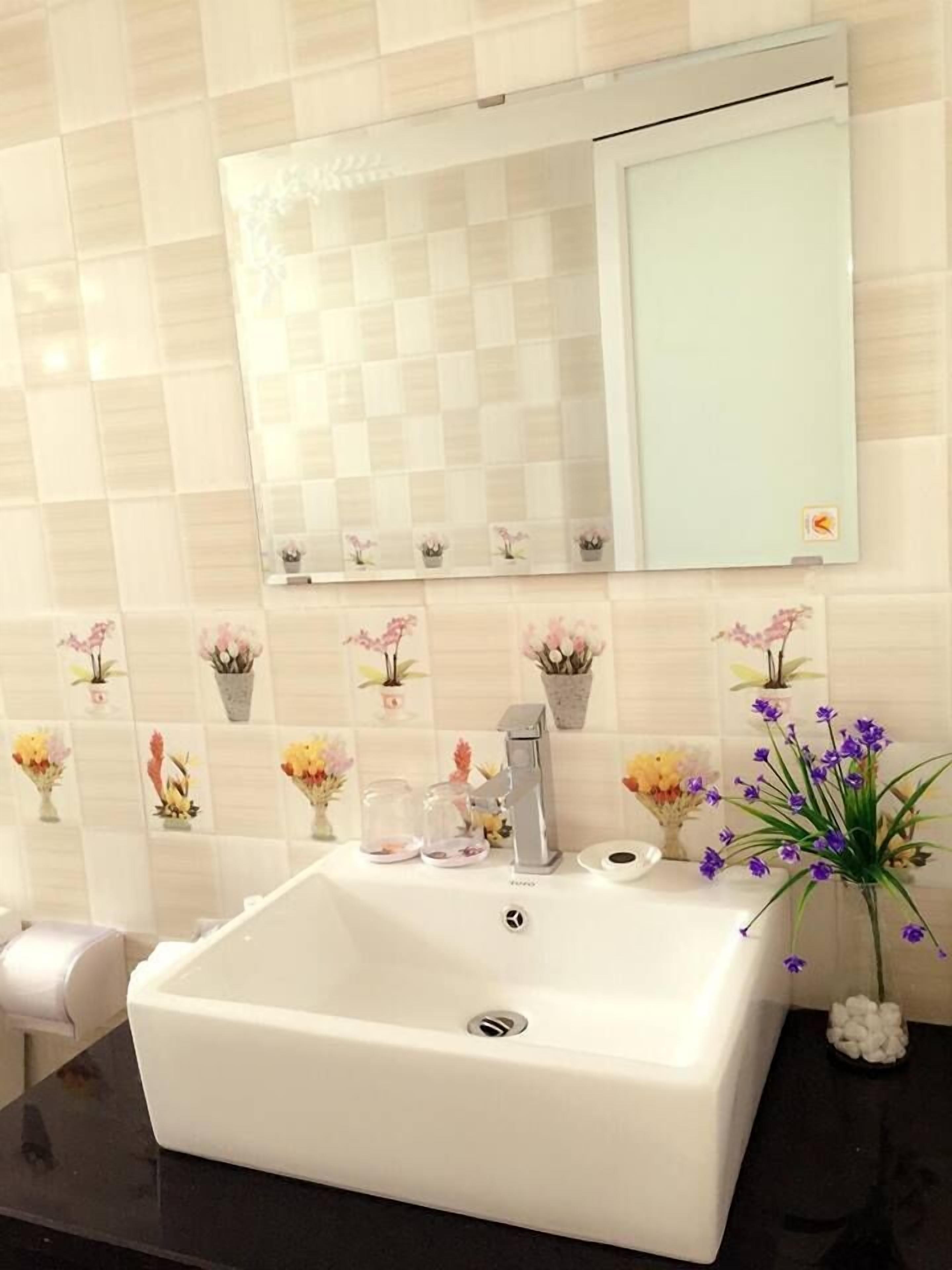 Un baño con lavamanos blanco, un espejo y azulejos decorativos.