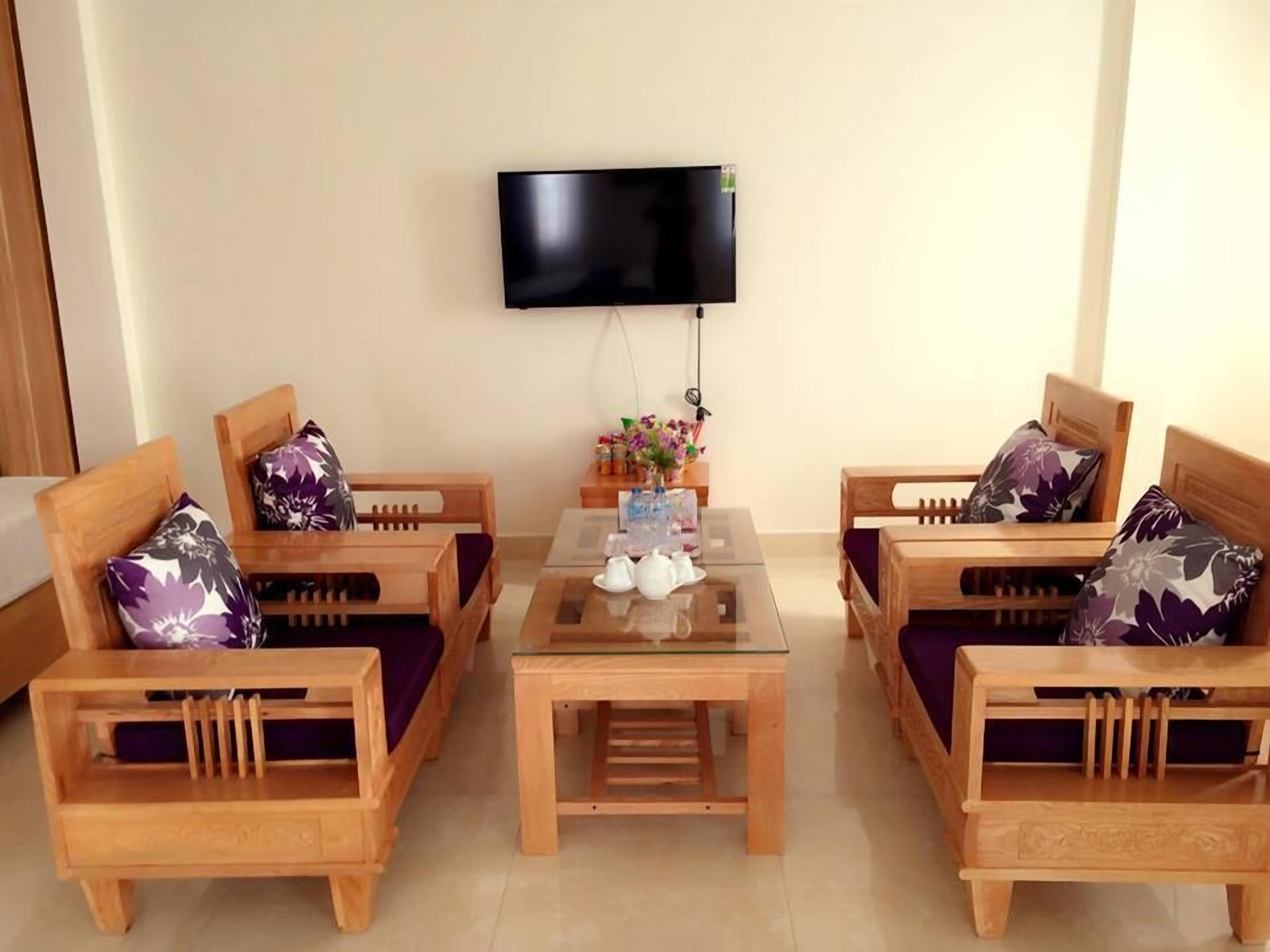 A room with two wooden sofas with purple floral cushions, a glass coffee table, and a flat-screen TV mounted on the wall.