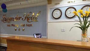 A hotel reception desk with a sign reading "Lavender Hotel Hai Phong Viet Nam" and clocks displaying times for Tokyo, New York, and Vietnam. - Lavender Hotel (Hai Phong)