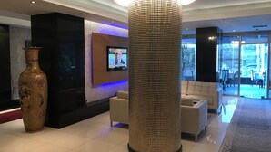 A lobby with a large decorative vase, a modern pillar, a flat-screen TV, and a seating area with a view of the outdoors. - Pen Hotel (Istanbul)