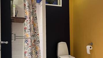A bathroom with a shower curtain, toilet, and a small shelf with a plant.
