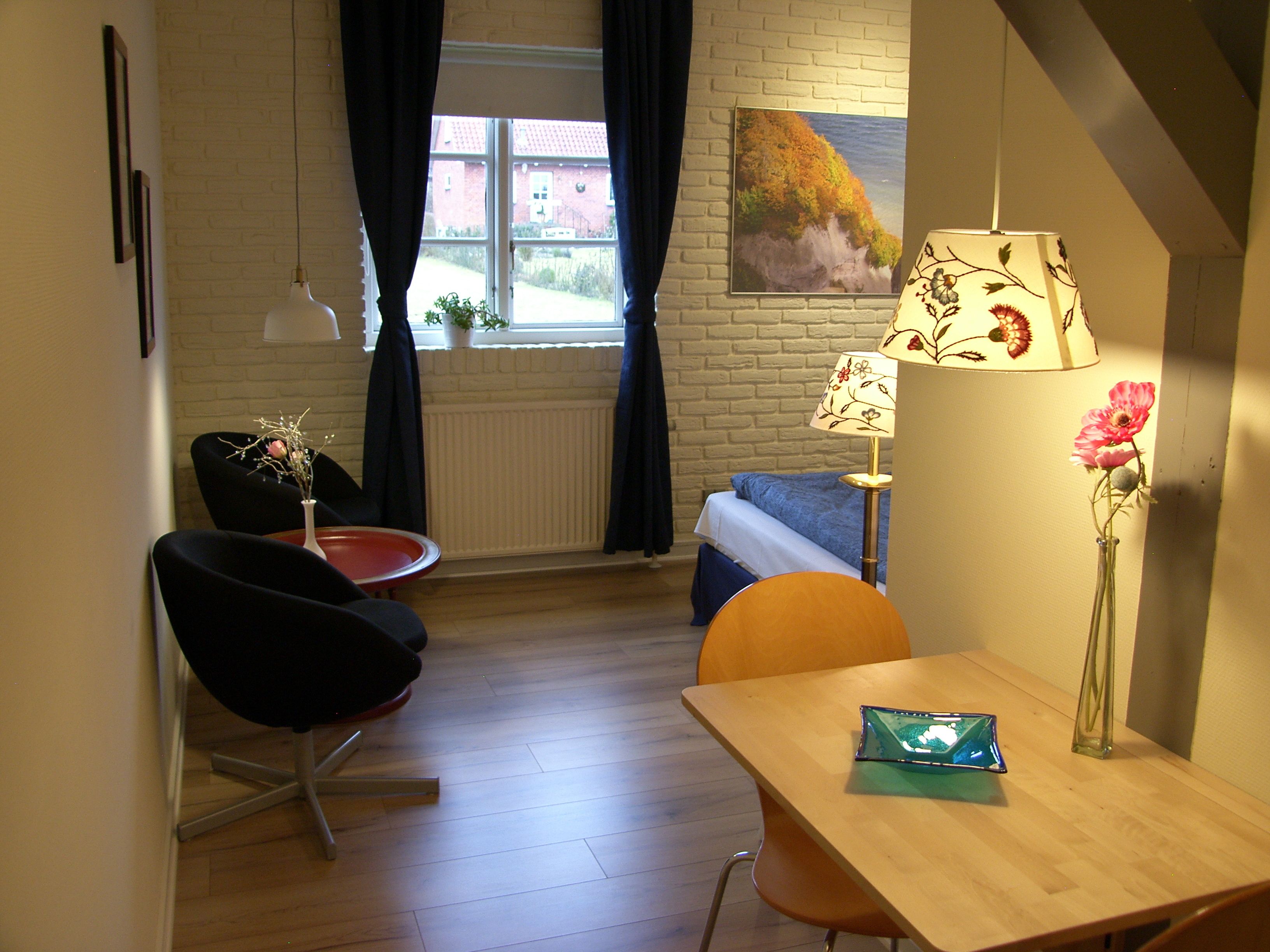 A room with a bed, a desk, a chair, a lamp, and a window with curtains.