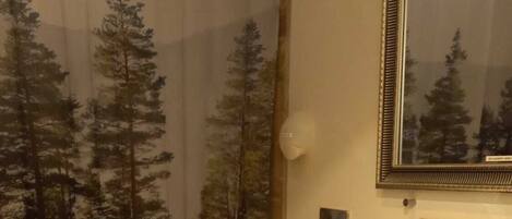 A bathroom with a shower curtain depicting trees, a toilet, a sink with a mirror, and a tiled floor.