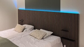 Un dormitorio moderno con cama, dos almohadas, una mesita de noche y estante en la pared.