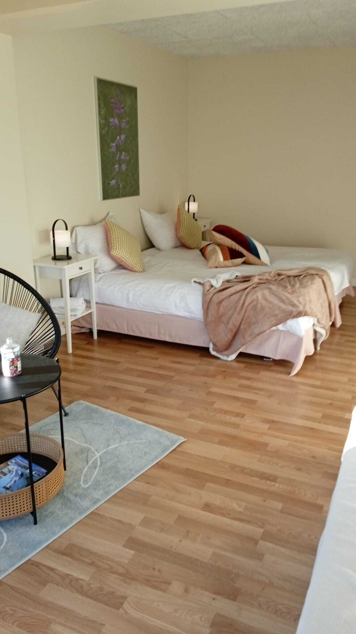 Een slaapkamer met een bed, nachtkastje, stoel en een klein tafeltje met een mandje.