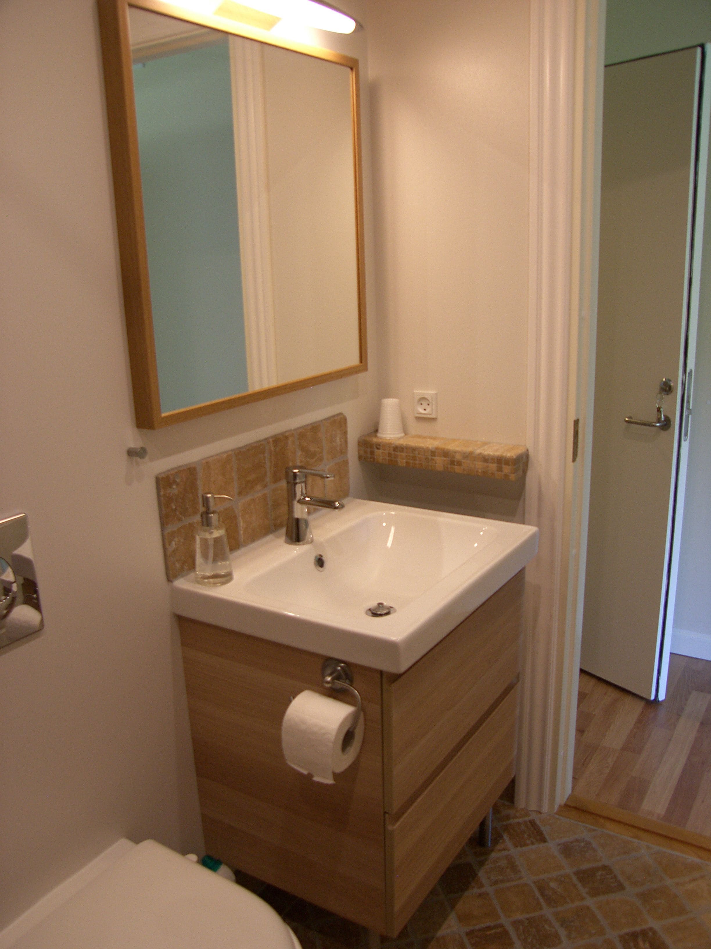 A bathroom with a white sink, a mirror, a towel dispenser, and a toilet.