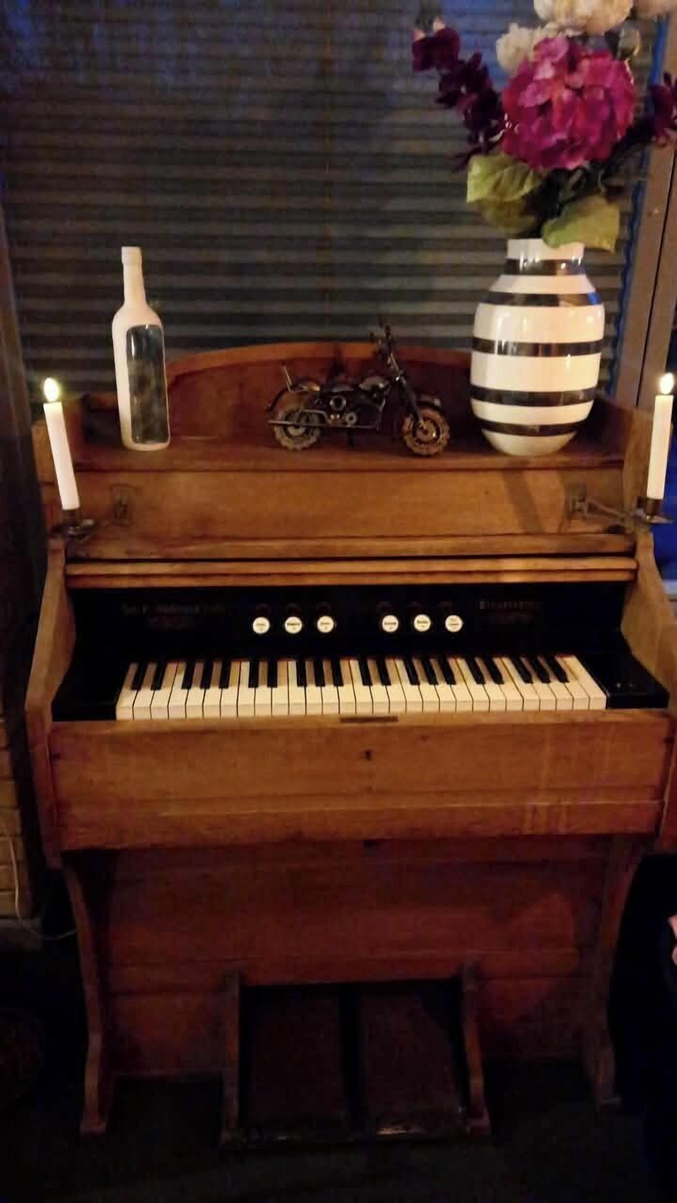 A wooden piano with a decorative vase and a motorcycle on top.