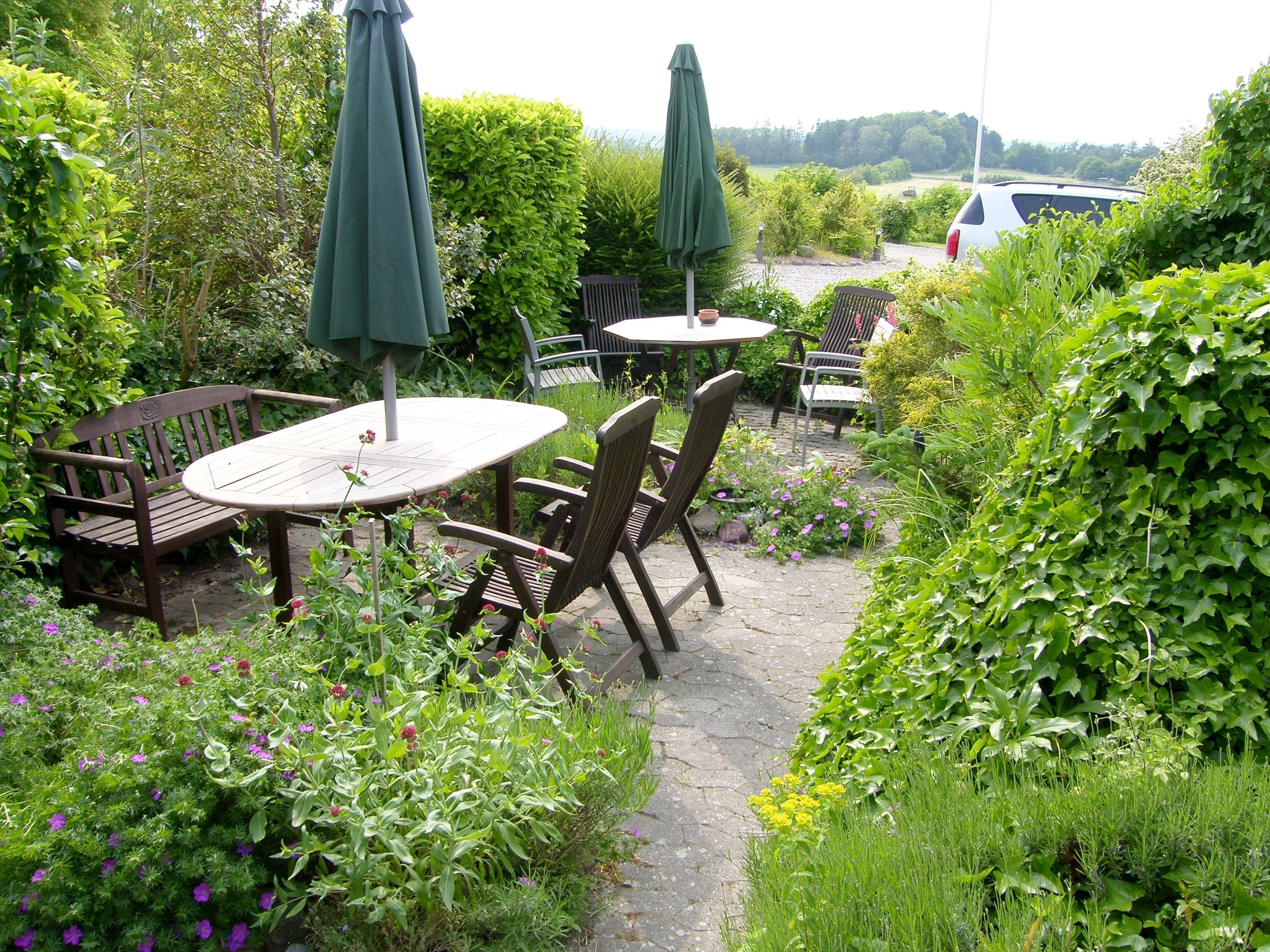 An outdoor patio area with round tables and chairs, surrounded by lush greenery and flowering plants.