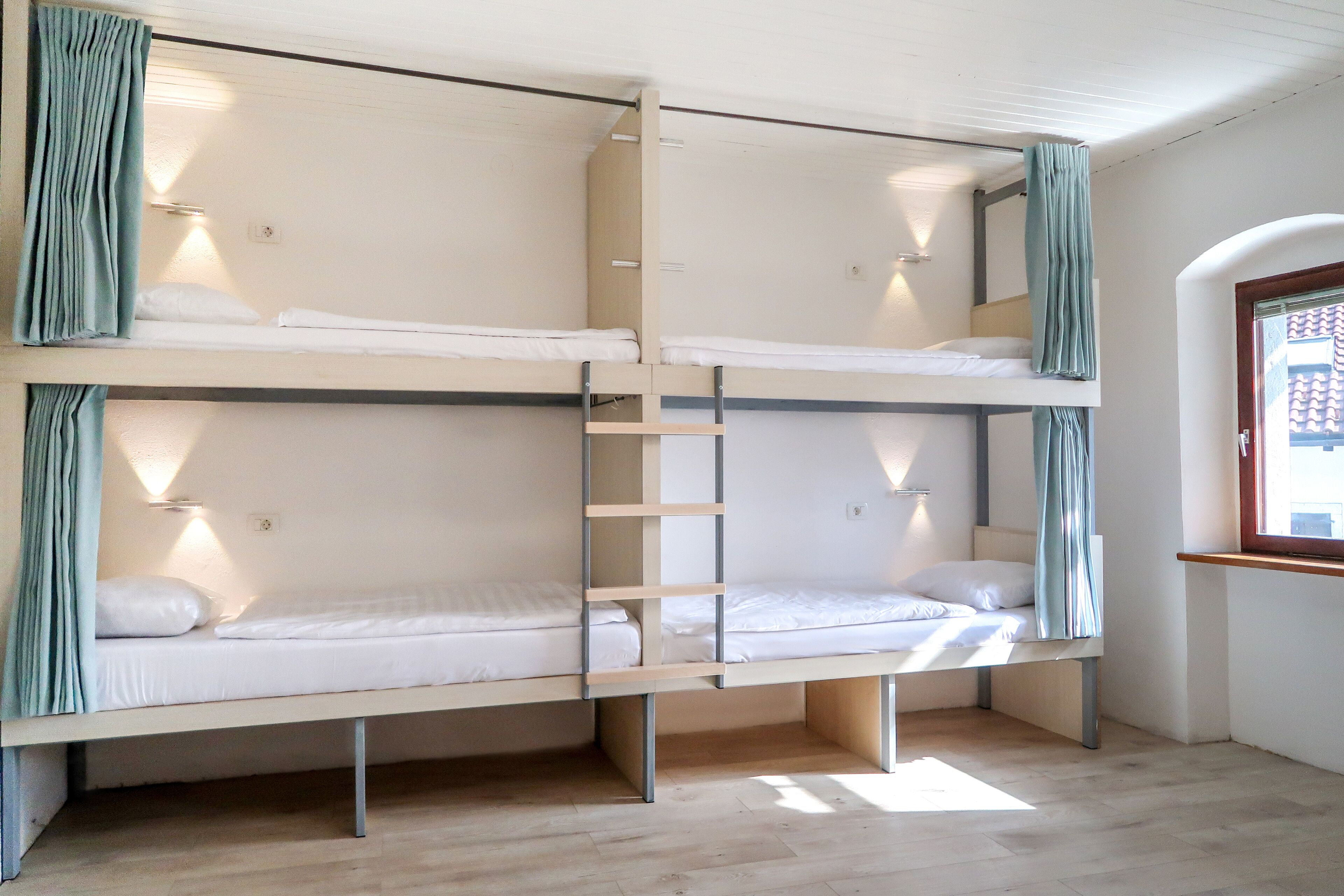 A bunk bed room with a ladder, a window with a view, and a wooden floor.