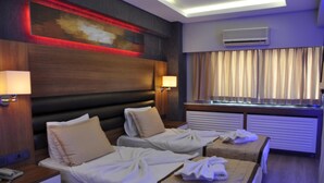 Habitación de hotel con dos camas, cada una con almohada y manta, una mesita de noche con lámpara y una ventana con cortinas.