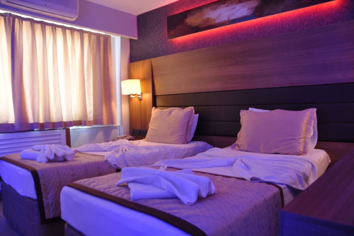 A hotel room with two beds, a nightstand with a lamp, and a large painting on the wall.