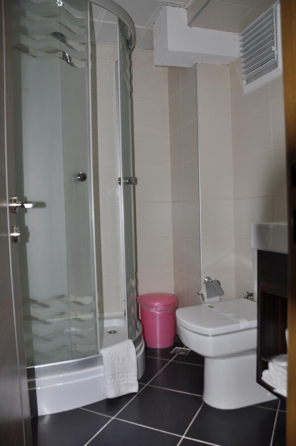 A bathroom with a glass-enclosed shower, a white toilet, and a pink trash bin. - Otel Kabacam (Izmir)