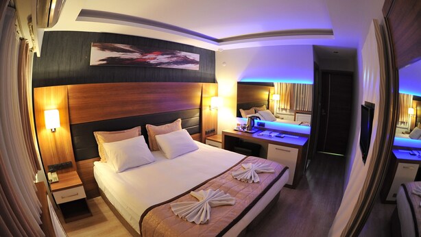 Una habitación de hotel con una cama grande, mesitas de noche, un escritorio y un espejo.