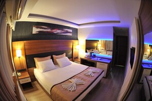 Una habitación de hotel con una cama grande, mesitas de noche, un escritorio y un espejo.
