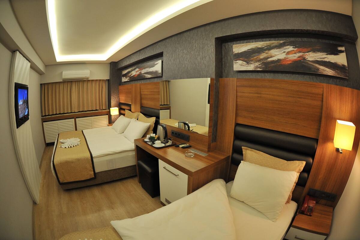 A hotel room with two beds, a desk, a mirror, and artwork on the walls.