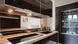 A modern kitchen with a central island, built-in oven, and a glass-fronted dining area with wine glasses. - Rent In Rome - Vatican Deluxe (Rome)