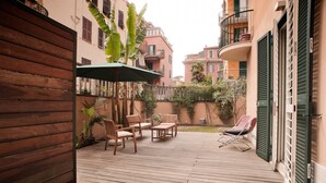 A wooden deck with outdoor furniture, a green umbrella, and a view of neighboring buildings. - Rent In Rome - Vatican Deluxe (Rome)