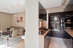 Une cuisine moderne dotée d’un four encastré, d’un coin repas avec une table en verre et des chaises, et d’un tableau accroché au mur.