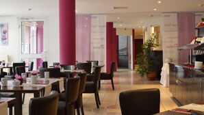 A modern restaurant interior with multiple dining tables and chairs, a large potted plant, and a kitchen area visible in the background. - Hotel Primula (Troisdorf)