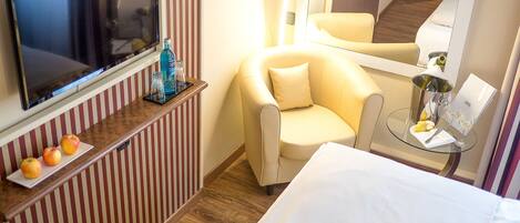 A hotel room with a bed, a chair, a small table with a bottle, glasses, and a plate of fruit.