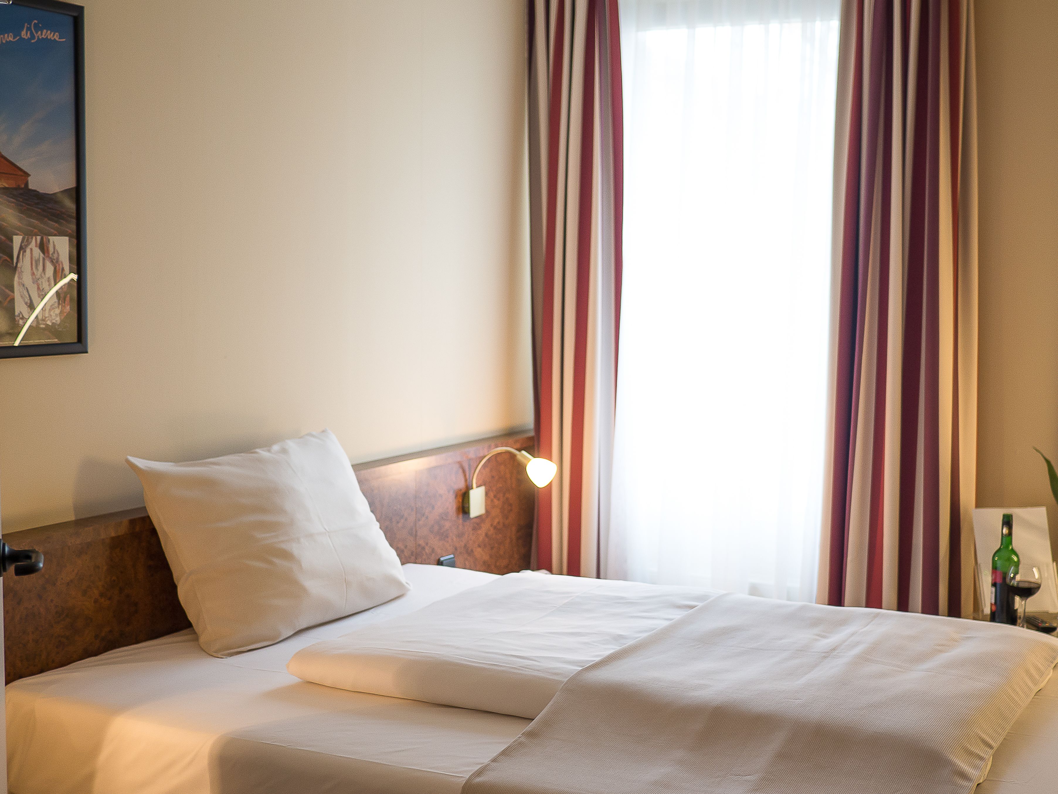 A neatly made bed with white linens, a headboard, and a bedside lamp.