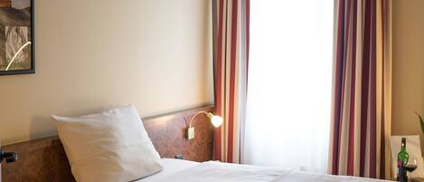 A neatly made bed with white linens, a headboard, and a bedside lamp.
