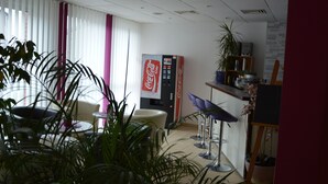 A modern office space with a vending machine, seating area, and potted plants. - Hotel Primula (Troisdorf)