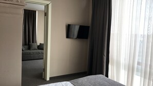 Habitación de hotel con cama, televisor montado en la pared y vistas al exterior a través de cortinas traslúcidas.