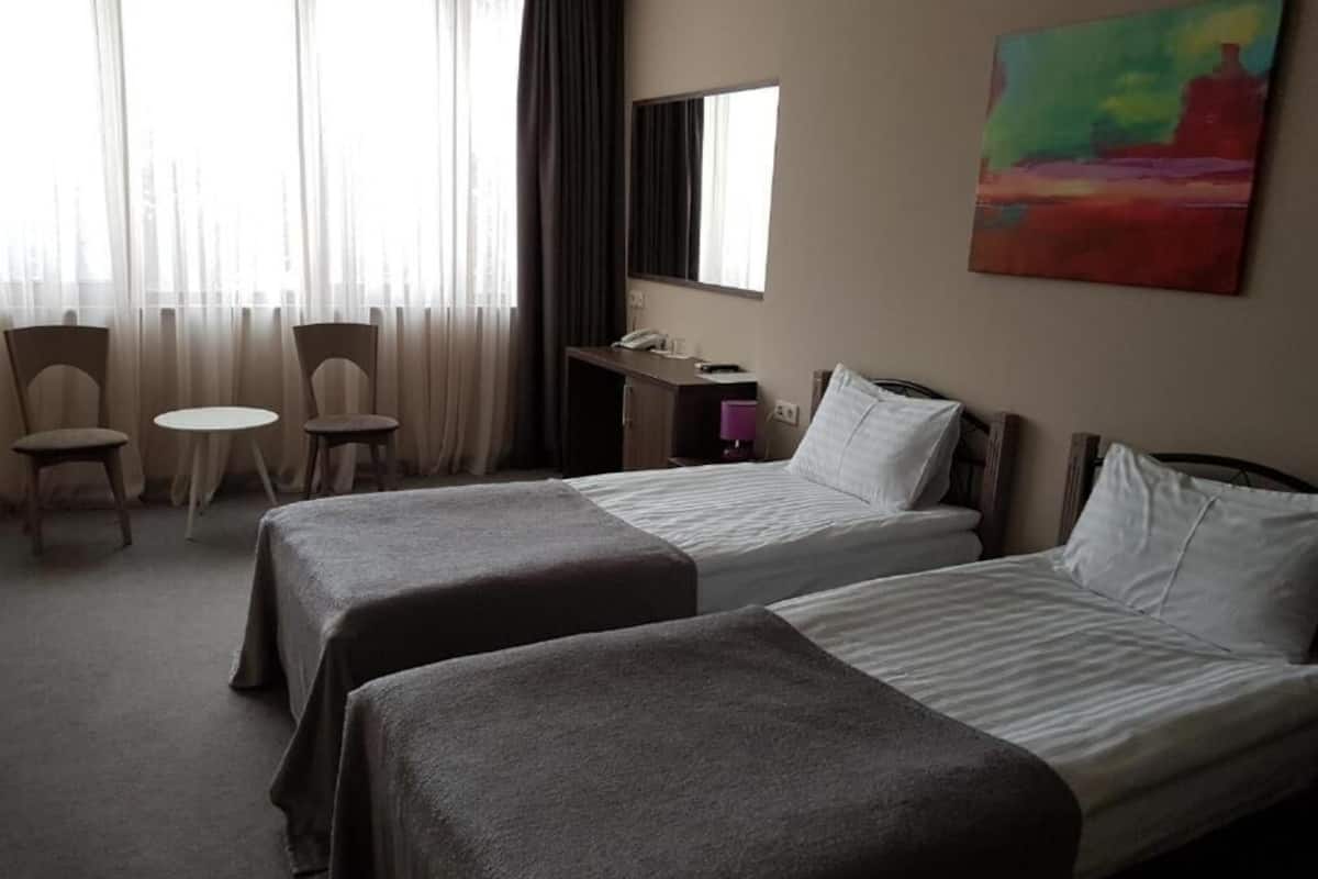 A hotel room with two single beds, a desk with a phone, a chair, and a painting on the wall.