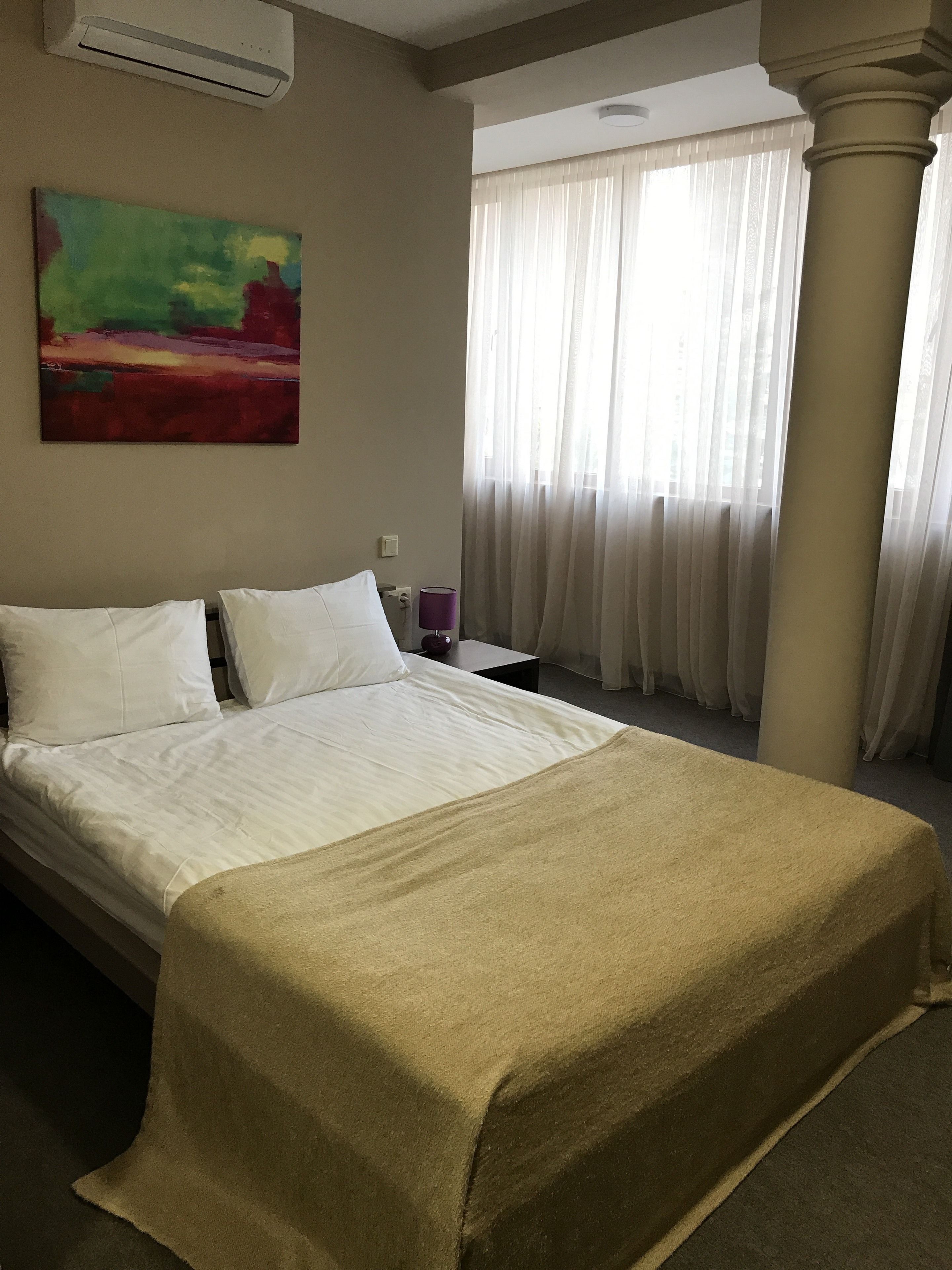 Quarto de hotel com cama, um quadro na parede, janela com cortinas e unidade de ar condicionado.